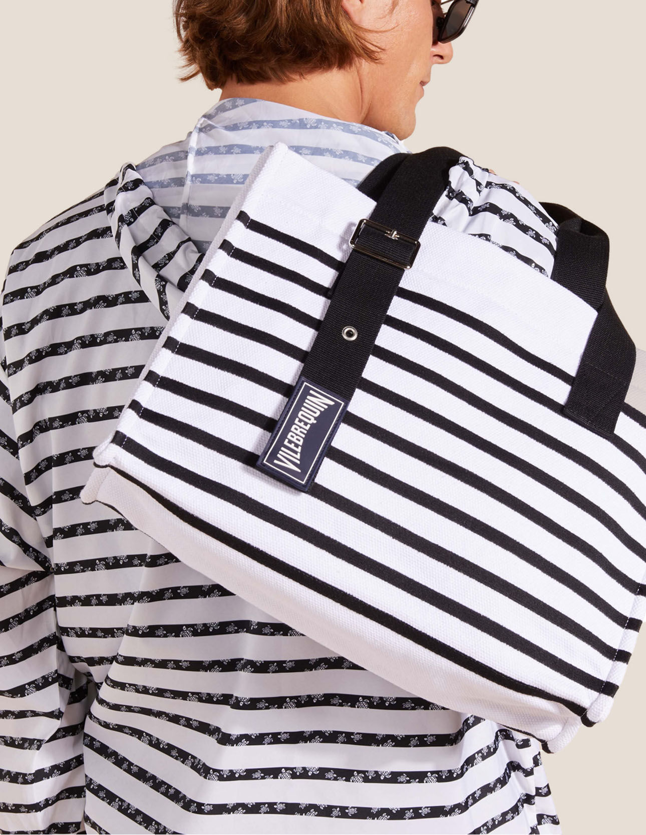 Man wearing a striped sailor shirt with a black and white striped beach bag.