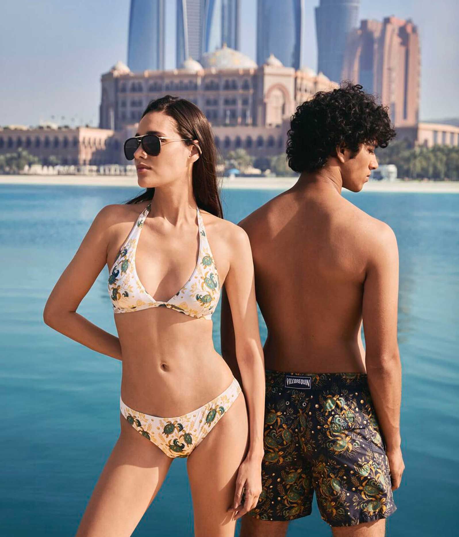 Couple posing in swimwear before sea and skyscrapers