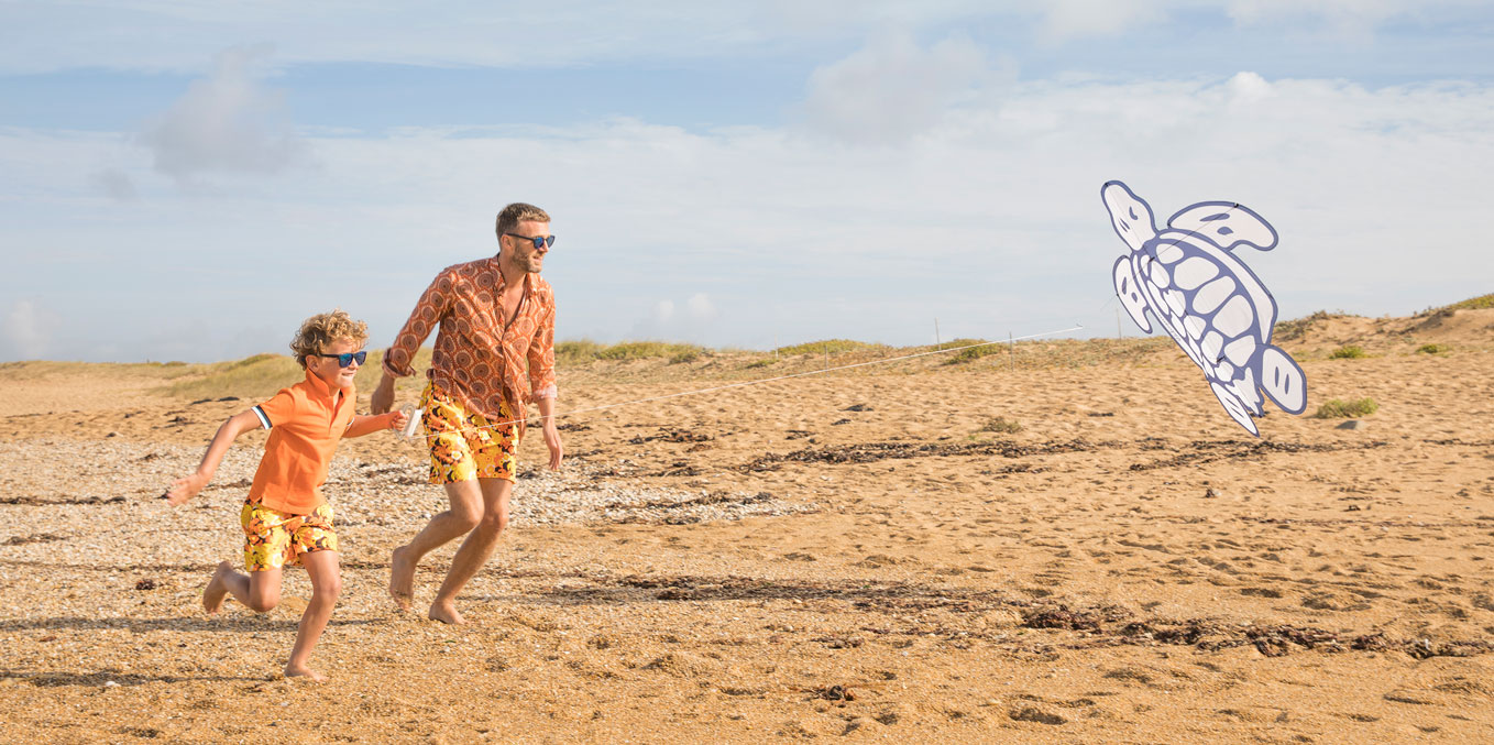 Father and son running on the beach with the Vilebrequin turtle kite