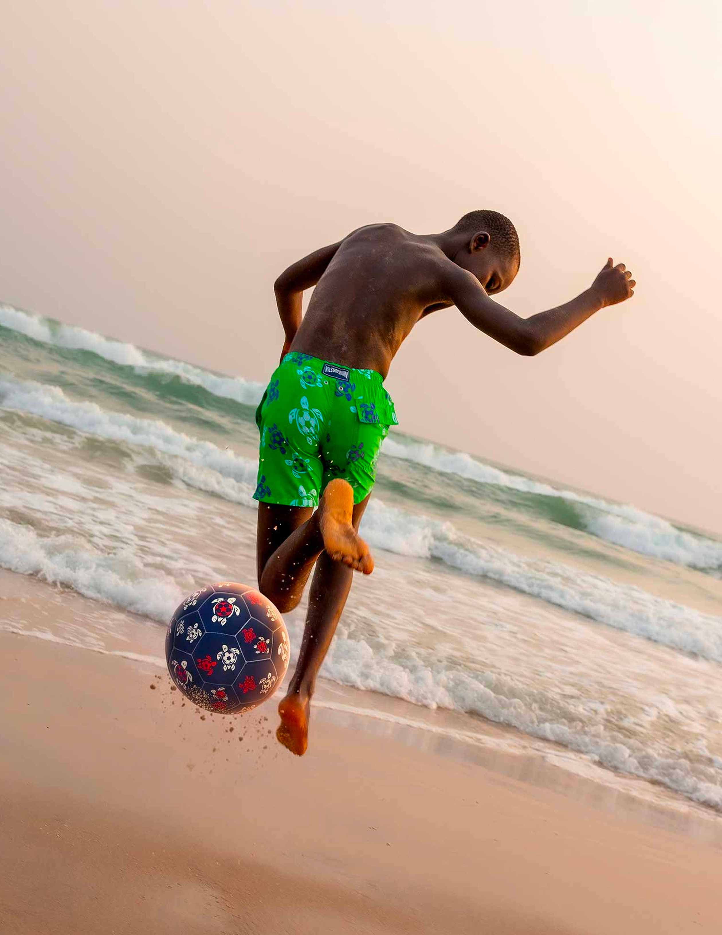 Un niño jugando al fútbol en la playa