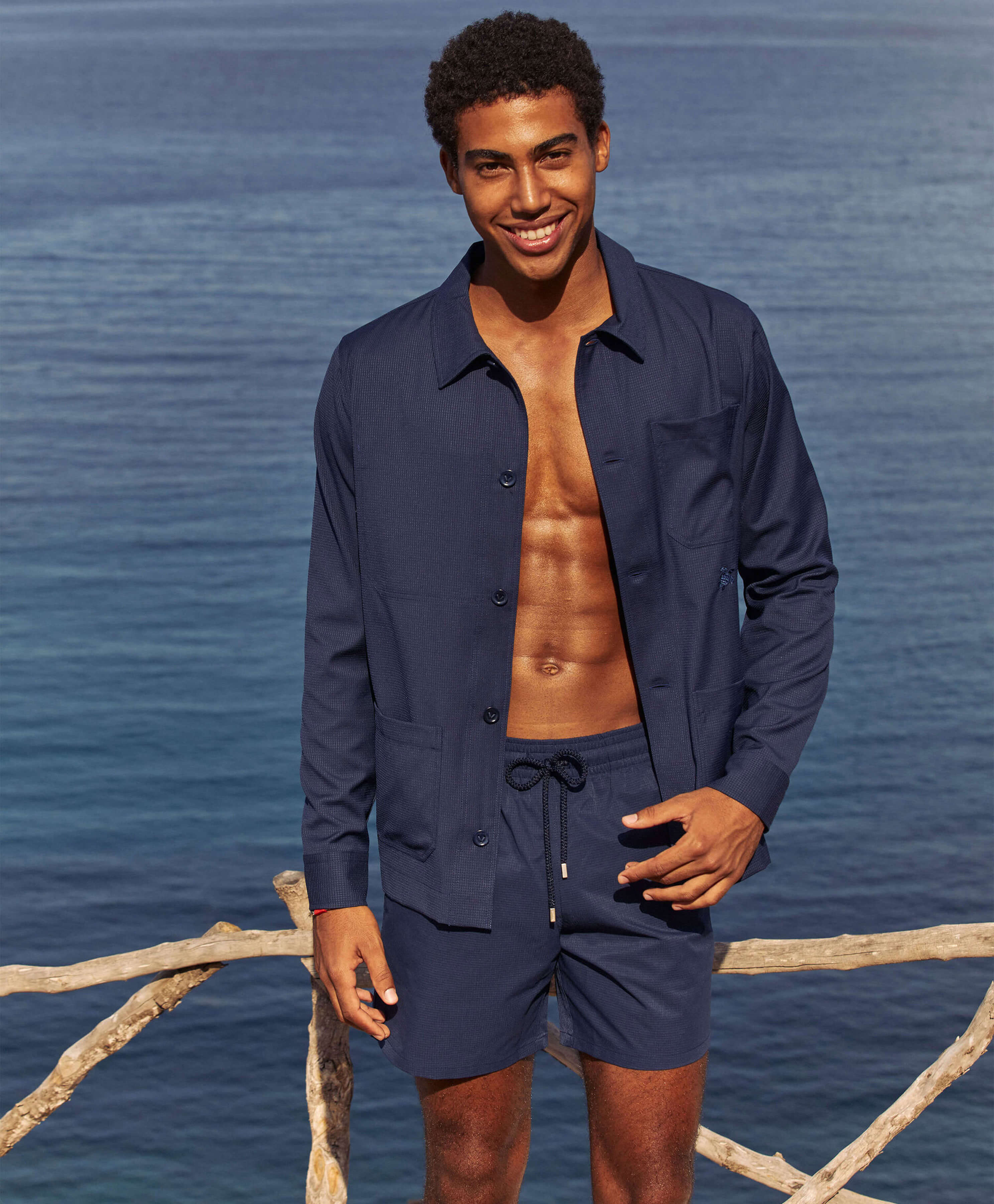 Ein Mann am Meer, der ein blaues Hemd und eine blaue Badehose trägt.