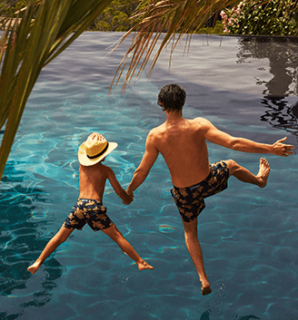 Father and Son jumping in pool wearing matching swimshorts