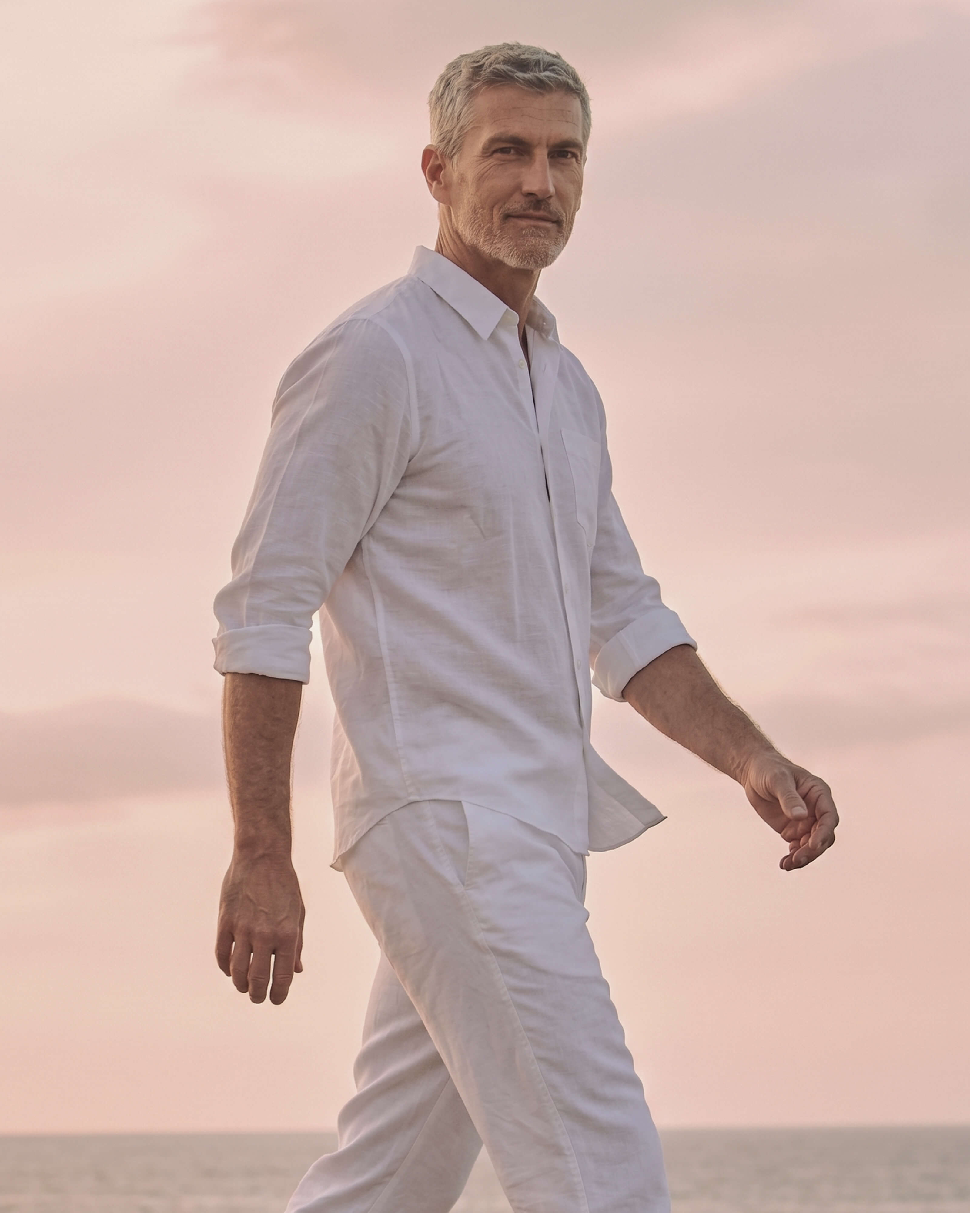 Man in White Linen A man wears a white linen shirt and trousers by the sea.