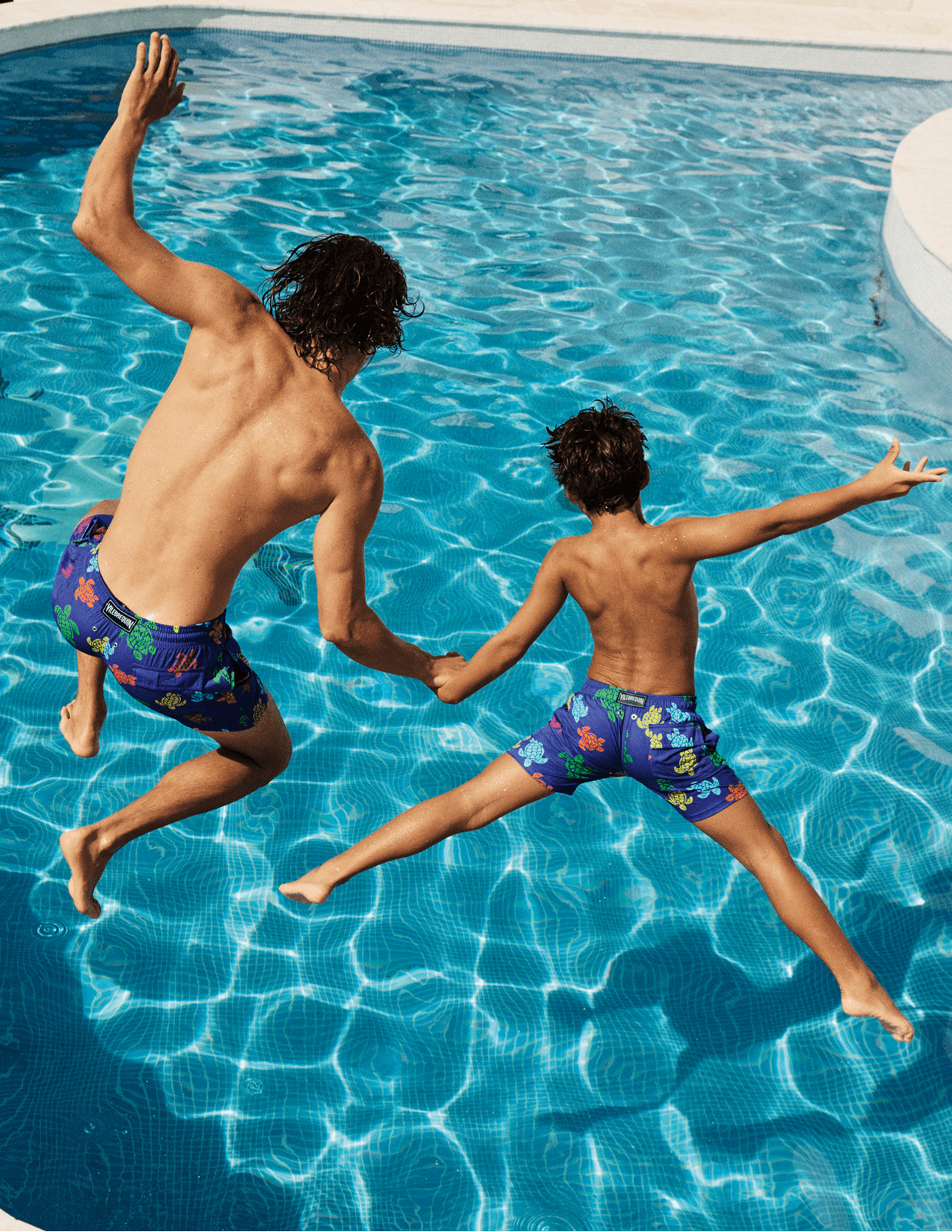 Dad and son jumping in a pool wearing the new Summer 25 collection